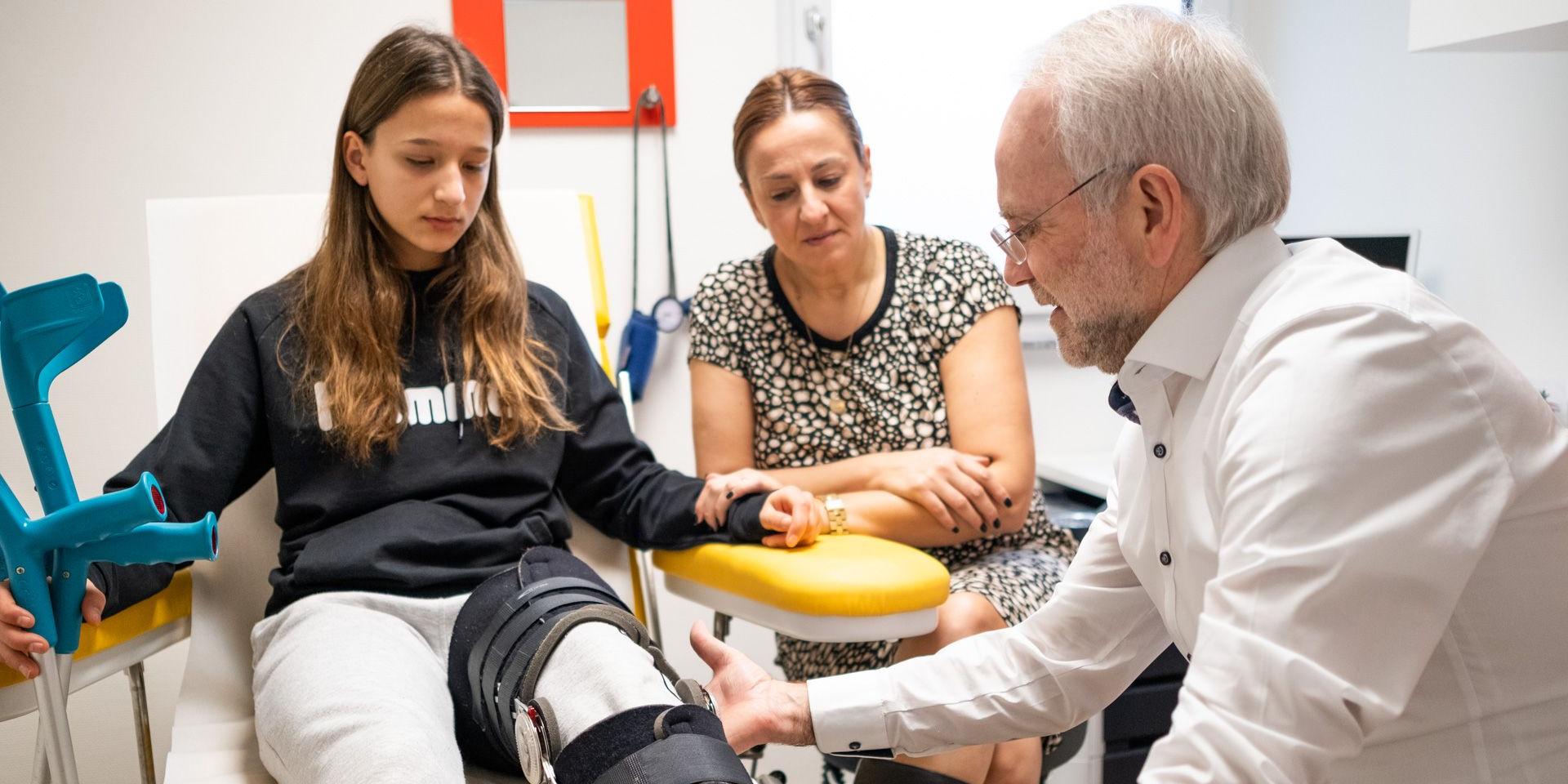 Herr Lintz untersucht den Fuß einer jungen Patientin, die von ihrer Mutter begleitet wird. Herr Lintz untersucht den Fuß einer jungen Patientin, die von ihrer Mutter begleitet wird.