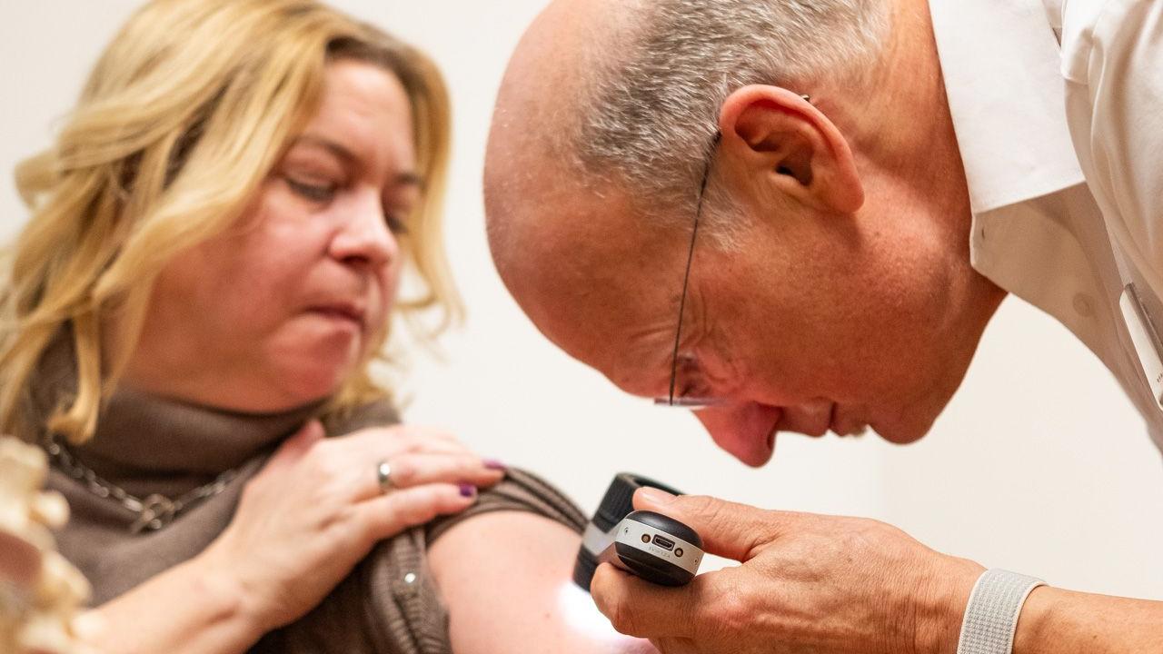 Herr Fischer untersucht bei einer Patientin Hautveränderungen.