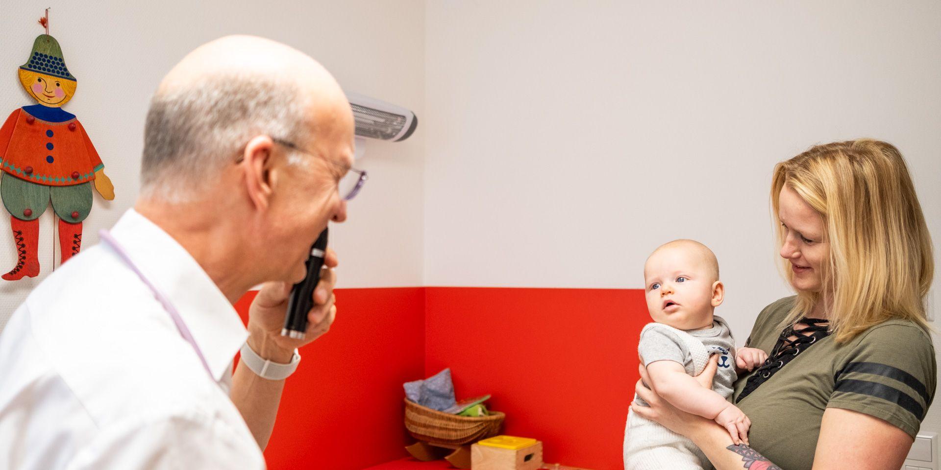 Arzt Joachim Fischer lenkt mit einer kleinen Lampe die Aufmerksamkeit eines Babys, das auf dem Arm der Mutter sitzt. Arzt Joachim Fischer lenkt mit einer kleinen Lampe die Aufmerksamkeit eines Babys, das auf dem Arm der Mutter sitzt.